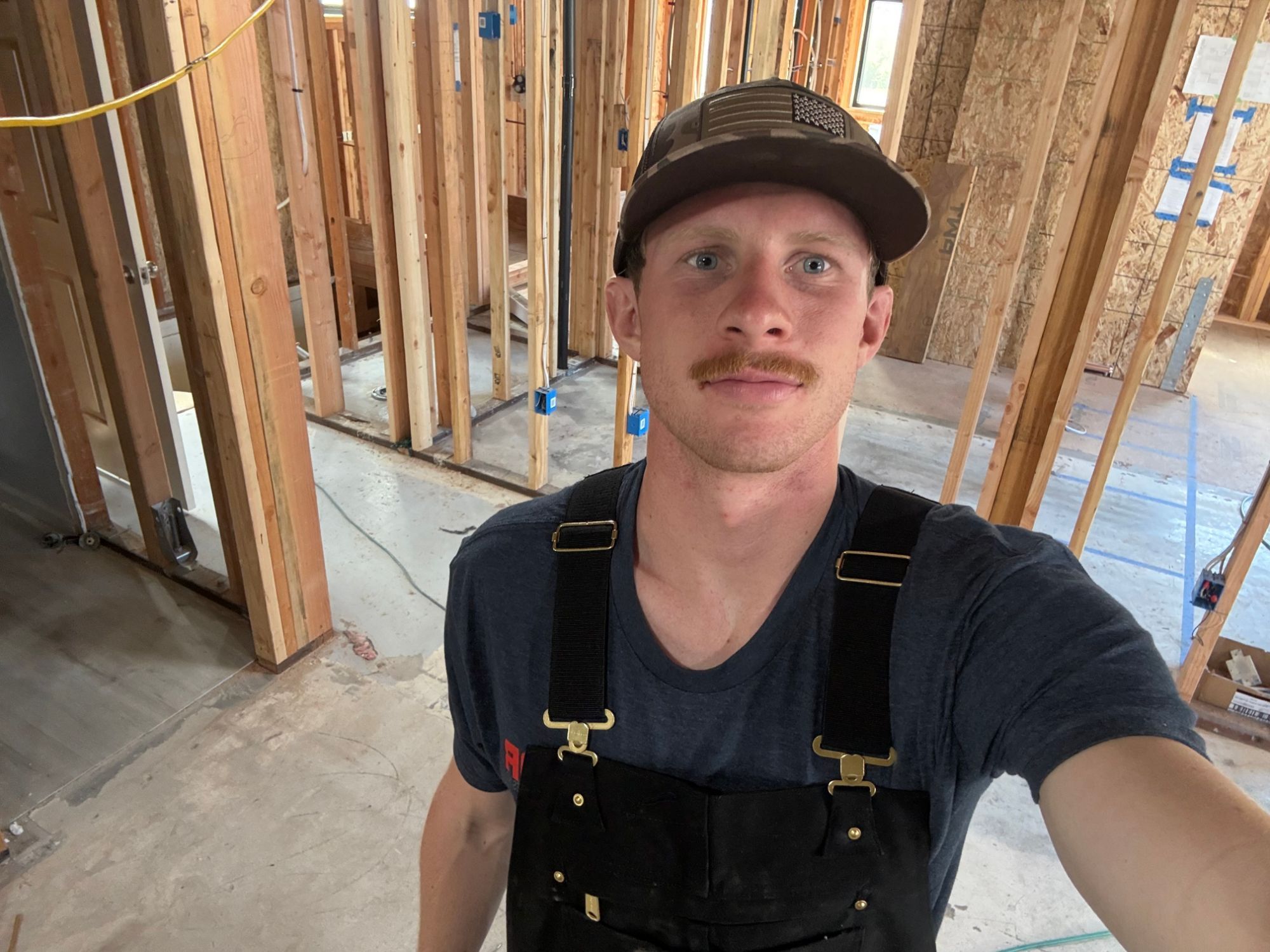 Jack Merickel on a framed-out job site in San Luis Obispo, wearing work overalls and a cap.